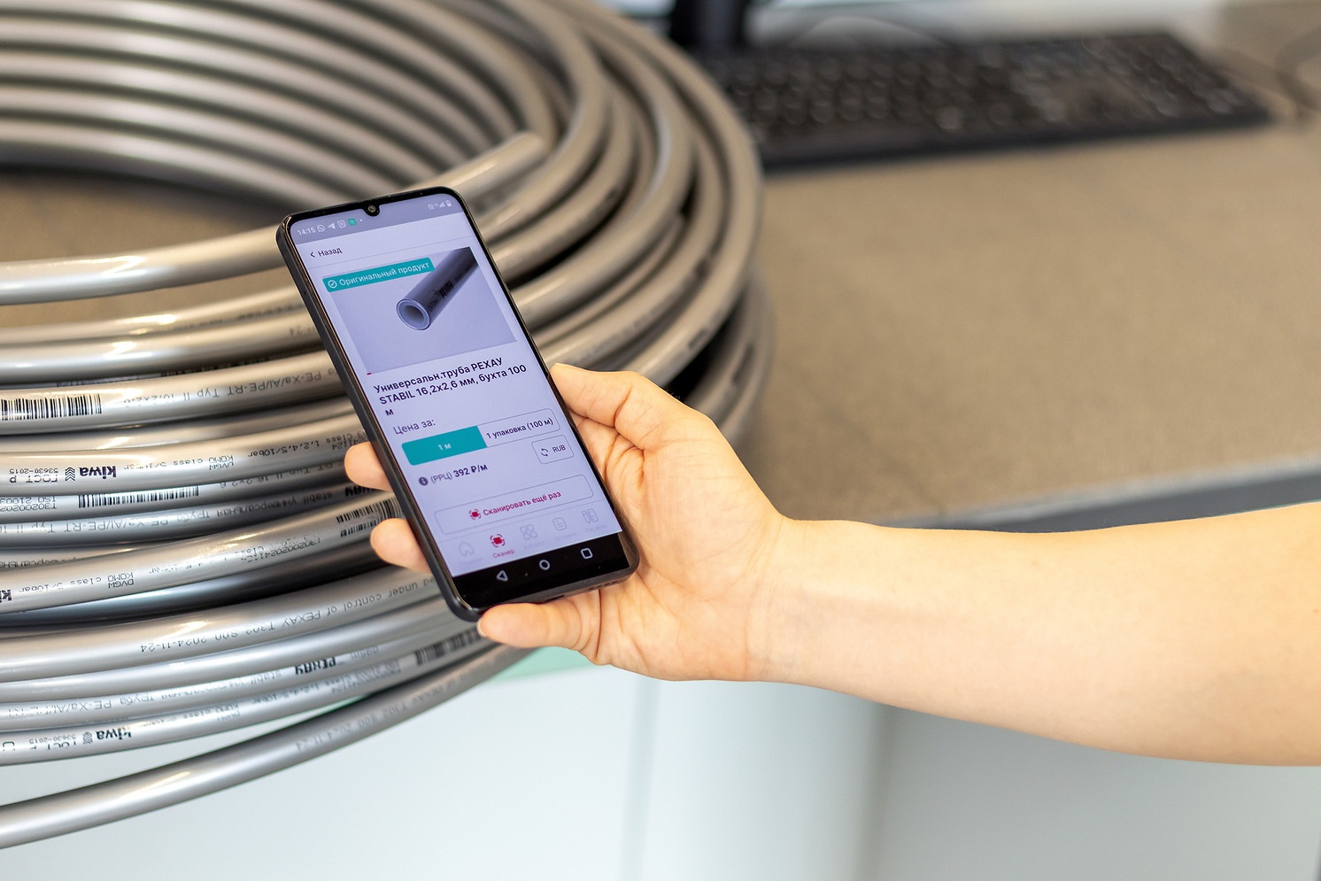 Рука со смартфоном сканирует QR-код на серой трубе РЕХАУ через фирменное приложение РЕХАУ Про Качество
