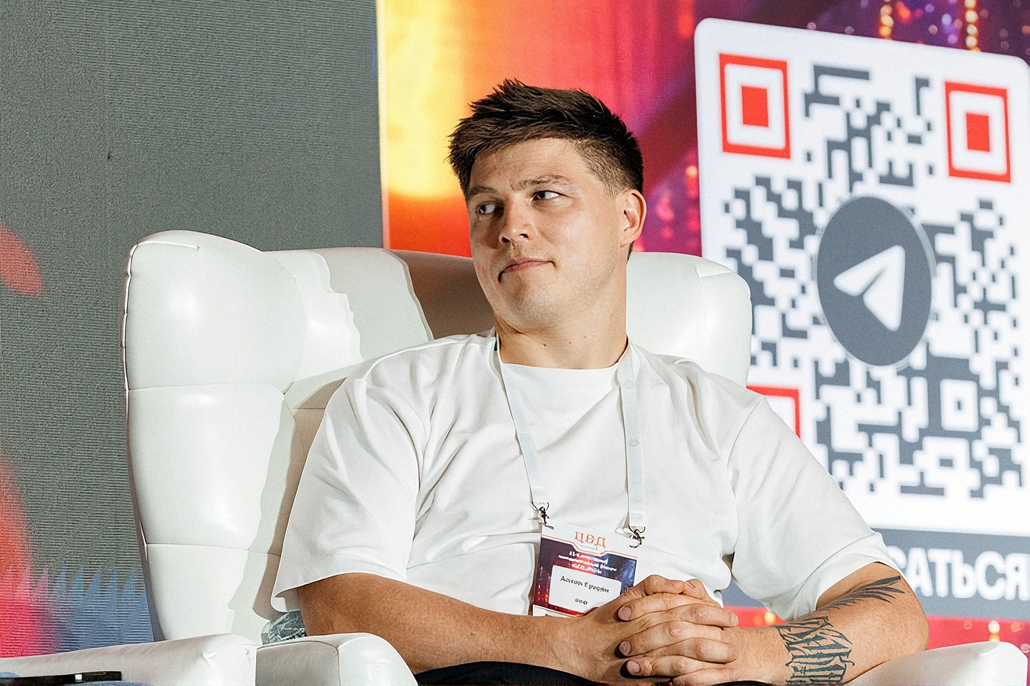 Спикер в белой футболке в кресле на сцене, позади экран с QR-кодом для подписки на канал