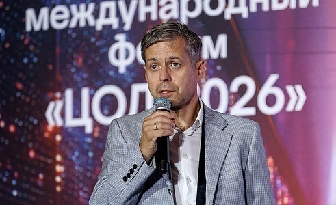 Спикер в светлом пиджаке говорит в микрофон на фоне заставки с названием форума