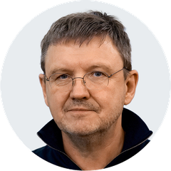 Мужчина в тёмной куртке с короткой стрижкой, портрет на светлом фоне, взгляд в камеру