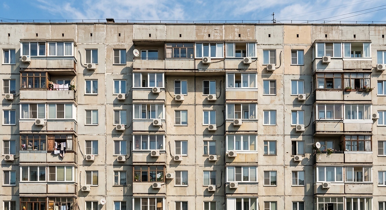 Многоэтажный панельный дом с рядами балконов, на фасаде у многих окон закреплены наружные блоки кондиционеров
