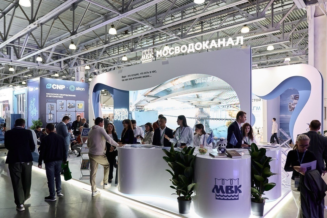 Стенд Мосводоканала с белыми изогнутыми конструкциями и стойкой ресепшен, у которой общаются посетители